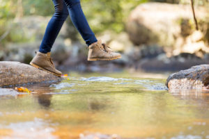 young woman hiking in mountain crossing stream